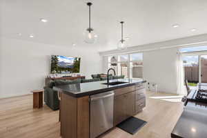 Kitchen featuring an island with sink, dishwasher, light wood-style floors, dark countertops, and a textured ceiling