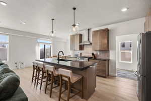 Kitchen with a breakfast bar, a center island with sink, stainless steel appliances, light wood finished floors, and decorative backsplash