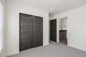 Unfurnished bedroom with light carpet, a closet, ensuite bathroom, and multiple windows