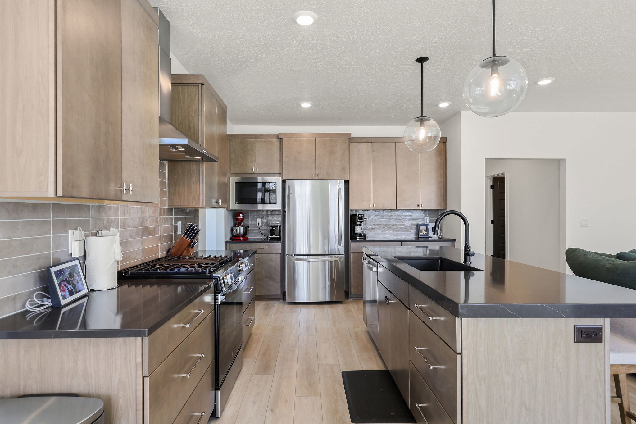 Kitchen featuring stainless steel appliances, light wood finished floors, an island with sink, hanging light fixtures, and a kitchen breakfast bar