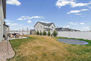 Fenced backyard featuring a patio area, a trampoline, a storage unit, and a residential view