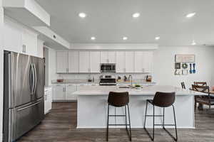 Kitchen featuring stainless steel appliances, white cabinetry, recessed lighting, a breakfast bar area, and a center island with sink