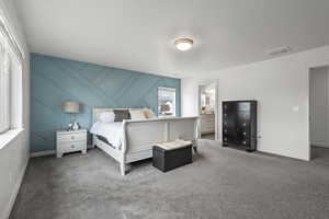 Bedroom with an accent wall, carpet, a decorative wall, ensuite bathroom, and a textured ceiling