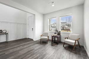 Sitting room featuring a decorative wall, dark wood-type flooring, and wainscoting