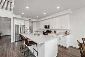 Kitchen featuring white cabinets, stainless steel appliances, a kitchen breakfast bar, a center island with sink, and light stone countertops