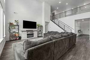 Living room featuring a high ceiling, dark wood-type flooring, a glass covered fireplace, and recessed lighting
