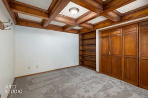 Unfurnished bedroom with carpet, coffered ceiling, and a closet