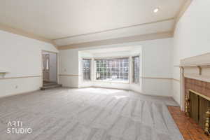 Unfurnished living room featuring carpet, a fireplace, vaulted ceiling, and ornamental molding