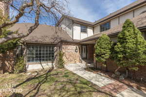 View of front facade with stucco siding, brick siding, a front yard, roof with shingles, and a patio