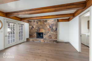 Unfurnished living room with beam ceiling, a stone fireplace, wood finished floors, a textured ceiling, and independent washer and dryer