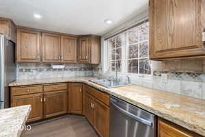Kitchen with wood finish cabinetry, stainless steel appliances, light stone counters, dark wood-type flooring, and decorative backsplash