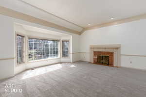 Unfurnished living room featuring light carpet, lofted ceiling, a fireplace, and ornamental molding