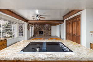 Kitchen with black electric stovetop, a textured ceiling, a ceiling fan, wood finish cabinetry, and a fireplace