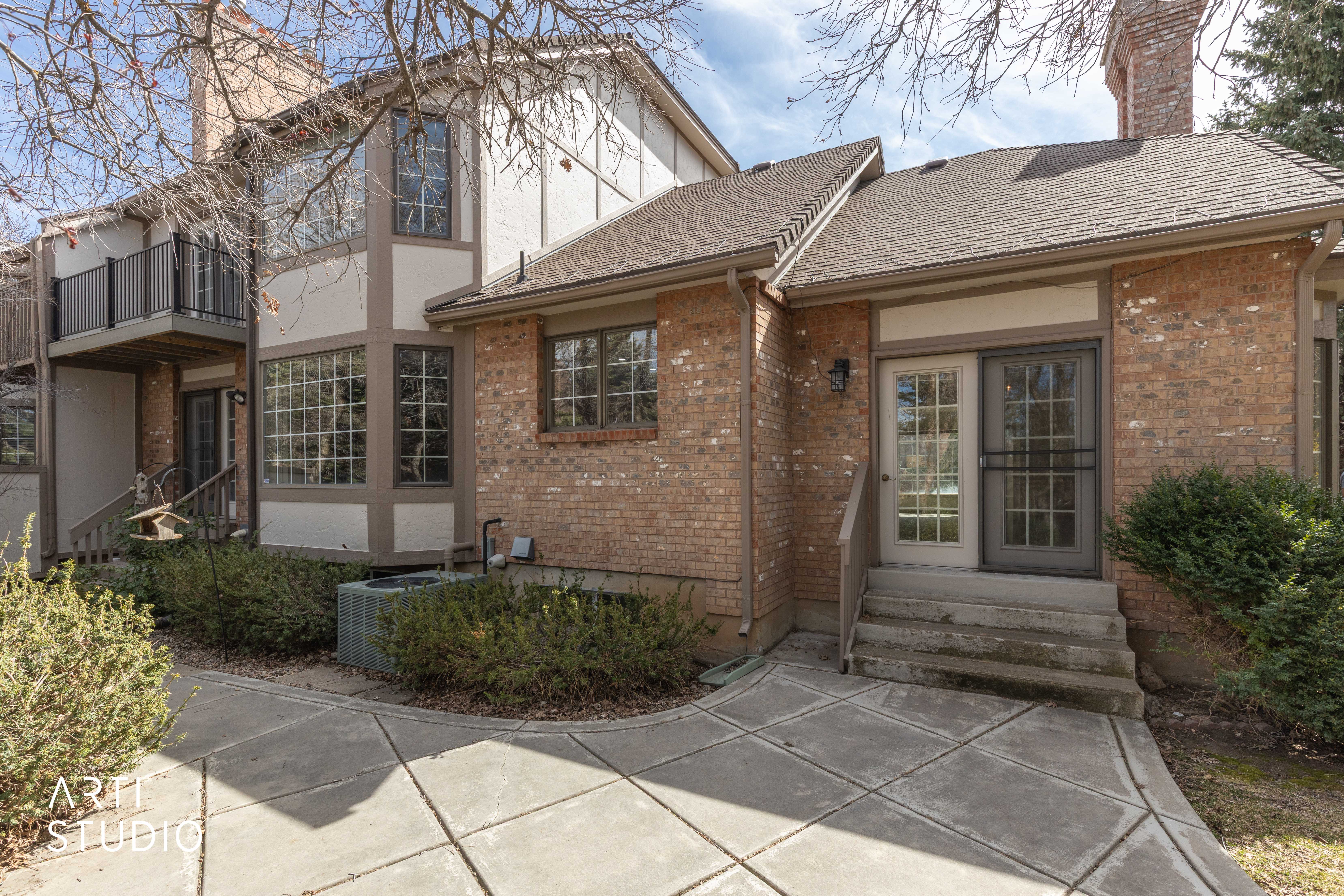 View of front of home with entry steps, a chimney, brick siding, stucco siding, and a patio area