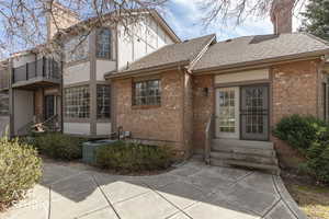 View of front of home with entry steps, a chimney, brick siding, stucco siding, and a patio area