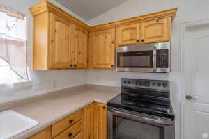 Kitchen with stainless steel appliances, light countertops, lofted ceiling, and light wood finish cabinetry