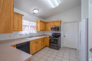 Kitchen featuring stainless steel appliances, light countertops, lofted ceiling, light tile patterned floors, and light wood finish cabinetry