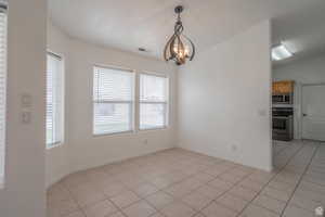 Unfurnished dining area featuring lofted ceiling, light tile patterned flooring, and hanging lights