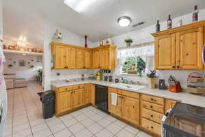 Kitchen featuring black appliances, light countertops, light tile patterned floors, and light wood finish cabinets