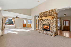 Main living room with view of stone fireplace and dining room with ceiling fan