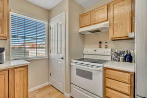 Kitchen with white electric range, light wood finish cabinetry, light countertops, light wood-style flooring, and freestanding refrigerator