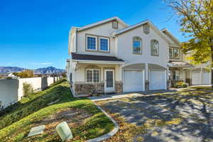View of front facade featuring stucco siding, stone siding, a garage, driveway, and a mountain view