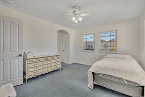 Bedroom with arched walkways, dark colored carpet, and ceiling fan