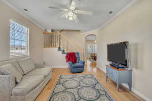 Living room featuring ceiling fan, arched walkways, light wood-style flooring, and ornamental molding