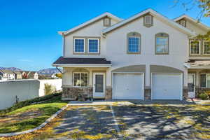 View of front facade with stucco siding, stone siding, asphalt driveway, an attached garage, and a mountain view