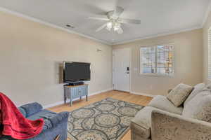 Living area with a ceiling fan, light wood-type flooring, and crown molding
