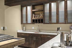 Kitchen featuring dark wood finish cabinetry, light stone counters, glass insert cabinets, and open shelves
