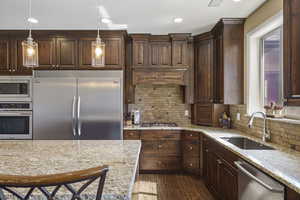 Kitchen with built in appliances, light stone countertops, tasteful backsplash, dark wood finish cabinets, and dark wood finished floors