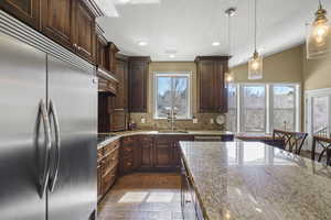 Kitchen with stainless steel appliances, dark wood-type flooring, light stone countertops, decorative light fixtures, and decorative backsplash