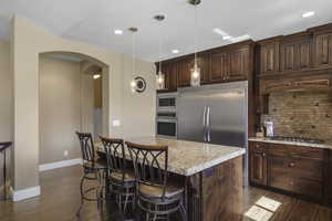 Kitchen featuring arched walkways, decorative backsplash, light stone countertops, dark wood-style floors, and built in appliances