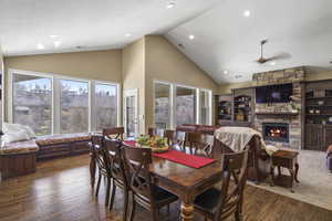 Dining room featuring a stone fireplace, healthy amount of natural light, a high ceiling, hardwood / wood-style floors, and ceiling fan