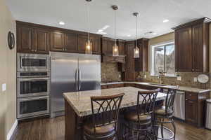 Kitchen featuring dark wood finish cabinets, built in appliances, a center island, a kitchen bar, and decorative light fixtures