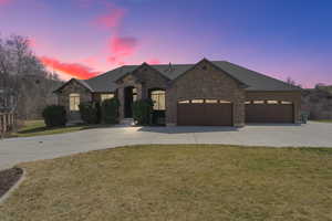 French provincial home with a yard, concrete driveway, stone siding, an attached garage, and a shingled roof
