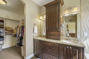Bathroom with double vanity, a spacious closet, ensuite bathroom, and light colored carpet