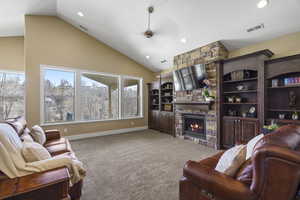 Carpeted living room with ceiling fan, recessed lighting, a stone fireplace, and lofted ceiling