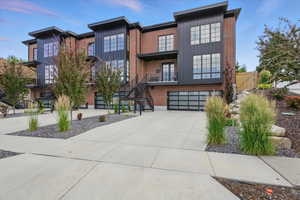 View of front of property with an attached garage, concrete driveway, brick siding, a balcony, and board and batten siding