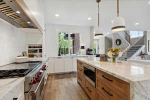 Kitchen featuring stainless steel appliances, dual tone cabinets, light stone counters, light wood-style flooring, and decorative light fixtures