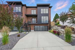 Contemporary house with an attached garage, driveway, a balcony, and brick siding