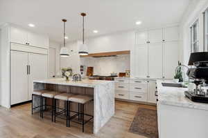 Kitchen with light stone countertops, paneled built in fridge, a kitchen island, and decorative light fixtures