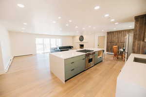 Kitchen featuring open floor plan, a large island, stainless steel appliances, light wood-style floors, and light stone counters