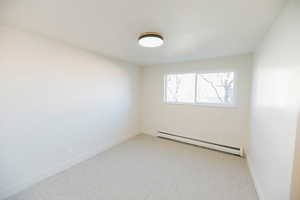 Empty room featuring a baseboard heating unit and light colored carpet