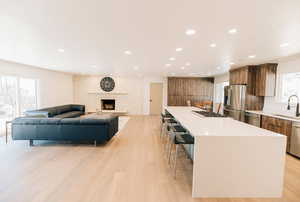 Kitchen with a large island, a kitchen bar, stainless steel appliances, light wood finished floors, and open floor plan