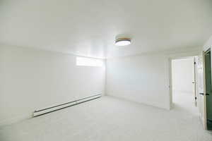 Empty room featuring a baseboard heating unit and light colored carpet