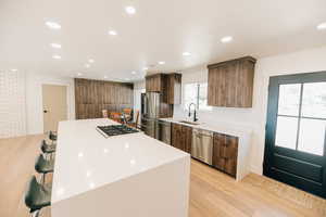 Kitchen with a breakfast bar area, a center island, modern cabinets, light wood finished floors, and light stone counters