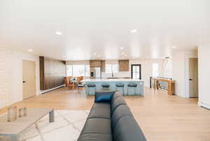 Living room with light wood finished floors, a baseboard radiator, and recessed lighting