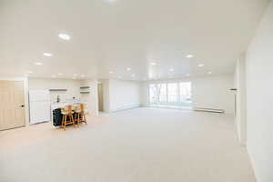 Basement with freestanding refrigerator, baseboard heating, light carpet, and recessed lighting